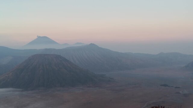 Breathtaking panoramic view of Mount Bromo volcano at sunrise, active crater emitting smoke over caldera, dramatic morning light, natural volcanic landscape, adventure travel and scenic destination