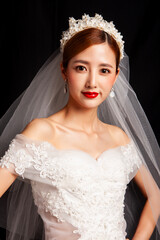 An elegant East Asian bride wearing an off-the-shoulder white lace wedding gown and a star-shaped pearl tiara, set against a solid black background. © jeson