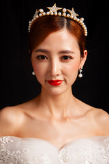 An elegant East Asian bride wearing an off-the-shoulder white lace wedding gown and a star-shaped pearl tiara, set against a solid black background. © jeson