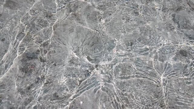 Clear tropical shallow water ripples over sandy seabed at Cemara Kecil island, sunlight caustic light patterns, natural ocean texture, serene marine surface, tranquil summer vacation background