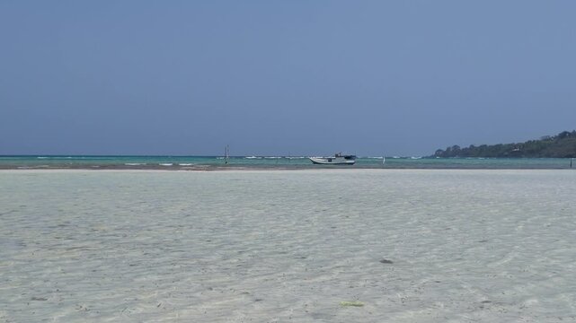 Clear shallow turquoise tropical ocean water at Karimunjawa island with a distant fishing boat on the horizon, calm seaside scenery, tranquil marine atmosphere, summer travel and holiday vibes