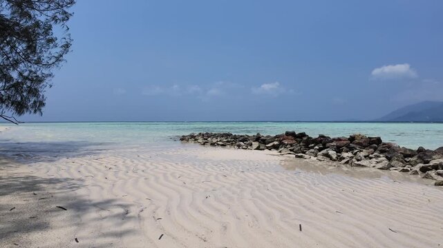 Clear turquoise water and rocky coastline at Cemara Kecil island, sandy beach with ripple texture, tropical paradise for summer travel, serene landscape for vacation getaway and outdoor exploration