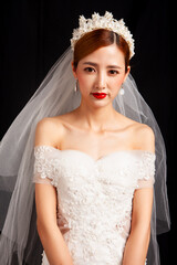 An elegant East Asian bride wearing an off-the-shoulder white lace wedding gown and a star-shaped pearl tiara, set against a solid black background. © jeson