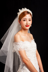 An elegant East Asian bride wearing an off-the-shoulder white lace wedding gown and a star-shaped pearl tiara, set against a solid black background. © jeson