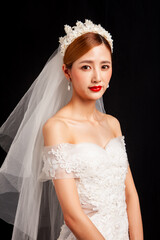 An elegant East Asian bride wearing an off-the-shoulder white lace wedding gown and a star-shaped pearl tiara, set against a solid black background. © jeson