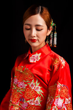 A young East Asian woman, dressed in exquisite traditional Chinese wedding attire and wearing classic hair accessories and makeup featuring red lips, embodies a festive wedding fashion style against a