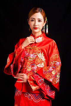 A young East Asian woman, dressed in exquisite traditional Chinese wedding attire and wearing classic hair accessories and makeup featuring red lips, embodies a festive wedding fashion style against a