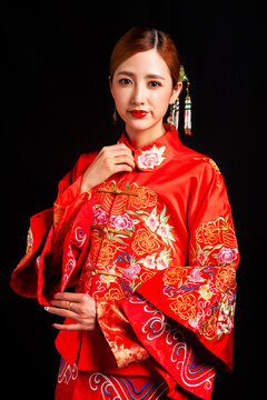 A young East Asian woman, dressed in exquisite traditional Chinese wedding attire and wearing classic hair accessories and makeup featuring red lips, embodies a festive wedding fashion style against a