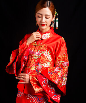 A young East Asian woman, dressed in exquisite traditional Chinese wedding attire and wearing classic hair accessories and makeup featuring red lips, embodies a festive wedding fashion style against a