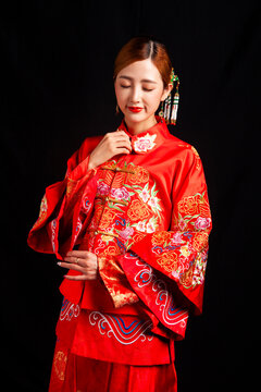 A young East Asian woman, dressed in exquisite traditional Chinese wedding attire and wearing classic hair accessories and makeup featuring red lips, embodies a festive wedding fashion style against a