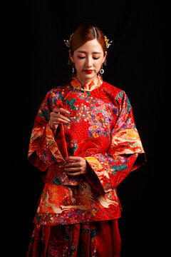 A young East Asian woman, dressed in exquisite traditional Chinese wedding attire and wearing classic hair accessories and makeup featuring red lips, embodies a festive wedding fashion style against a