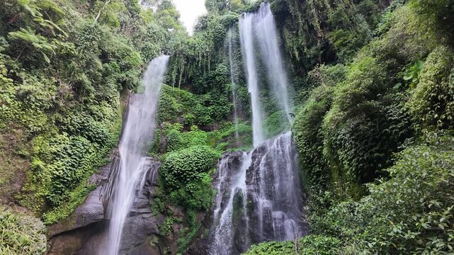 Dual cascading waterfall at Sekumpul in Bali surrounded by dense lush tropical foliage, jungle nature scenery, refreshing environment, peaceful vacation, travel destination, wild landscape scenery