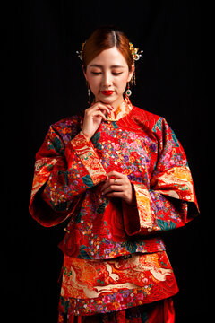 A young East Asian woman, dressed in exquisite traditional Chinese wedding attire and wearing classic hair accessories and makeup featuring red lips, embodies a festive wedding fashion style against a