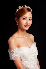 An elegant East Asian bride wearing an off-the-shoulder white lace wedding gown and a star-shaped pearl tiara, set against a solid black background. © jeson