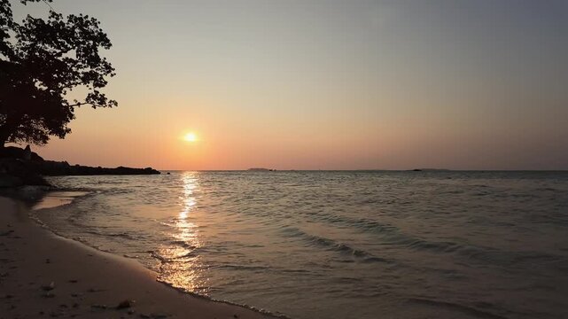 Golden sunset over tropical coastline with gentle waves lapping sandy beach, serene atmosphere, tranquil landscape, nature relaxation, travel scenery, island getaway, evening horizon. Time lapse