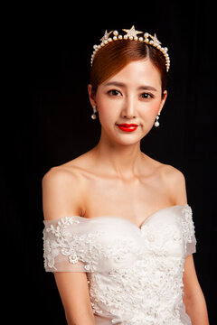 An elegant East Asian bride wearing an off-the-shoulder white lace wedding gown and a star-shaped pearl tiara, set against a solid black background.