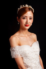 An elegant East Asian bride wearing an off-the-shoulder white lace wedding gown and a star-shaped pearl tiara, set against a solid black background. © jeson