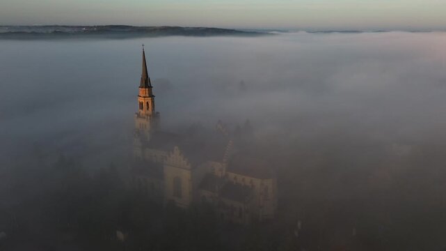 Church in the morning mist, village amidst the clouds, drone view.