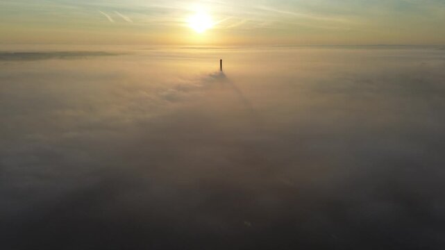 A solitary smokestack amidst morning fog and clouds &mdash; a drone view.