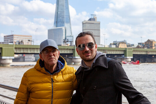 Two men posing by river thames with the shard and london bridge in background