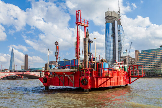 Red construction barge operating on river thames with london skyline in background