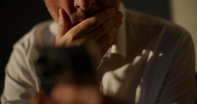 Close-up of a man's face holding a smartphone out in front of him, dramatic shadow and warm side lighting, focused expression. 4K.