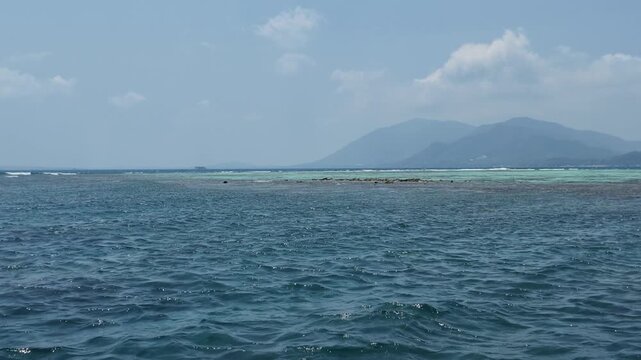 Seascape view of crystal clear blue ocean water with distant tropical mountains, horizon line, waves, serene atmosphere, travel and tourism destination, nature landscape, sunny daylight outdoors