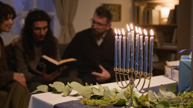 Caucasian adults celebrating Hanukkah and reading religious book behind burning menorah on table. Footage suitable for Jewish holiday marketing, winter faith campaigns and cultural storytelling