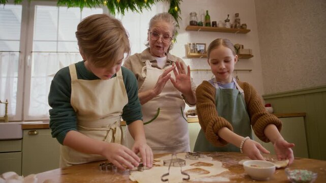 Senior Caucasian woman guiding Caucasian children cutting dough with cookie cutters. Clip suitable for festive culinary branding and family lifestyle commercials