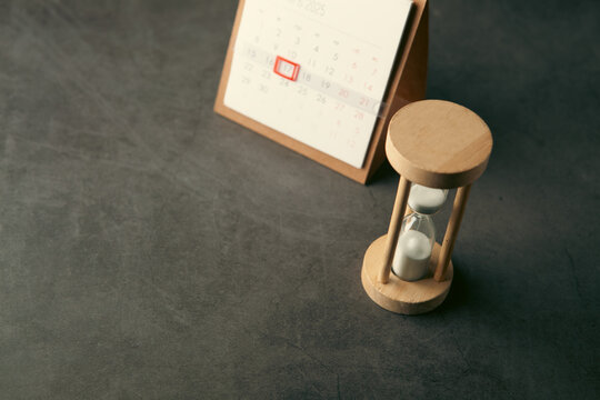 An hourglass and a calendar on the desk.
