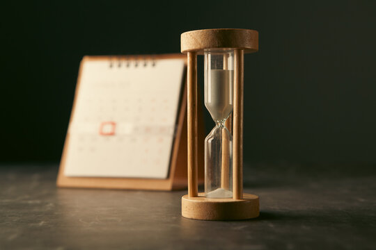 An hourglass and a calendar on the desk.