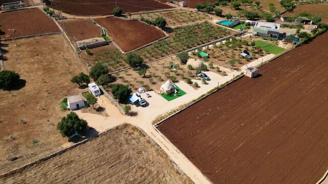 A high aerial view captures the rural Puglia countryside near Polignano a Mare, showcasing distinct red soil fields, scattered olive trees, and stone walls stretching towards the deep blue Adriatic