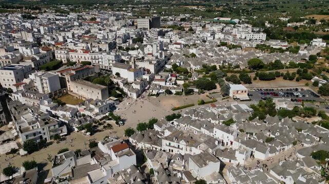 A breathtaking high aerial view of Alberobello in Puglia, Italy, revealing thousands of iconic white trulli huts with conical stone roofs. The historic UNESCO town stretches across the landscape