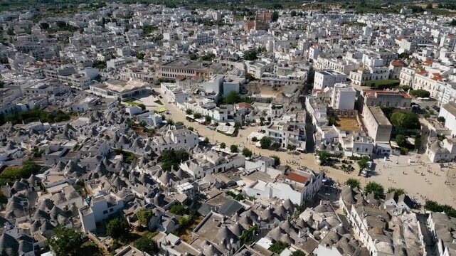 A breathtaking high aerial view of Alberobello in Puglia, Italy, revealing thousands of iconic white trulli huts with conical stone roofs. The historic UNESCO town stretches across the landscape