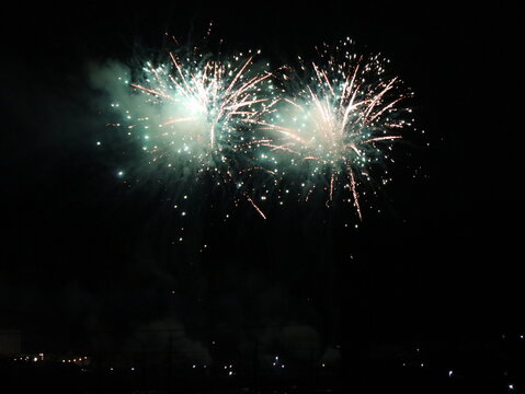 Twin green and gold fireworks exploding side by side in the night sky at a Japanese fireworks festival