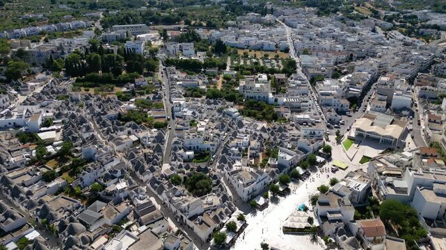 A breathtaking high aerial view of Alberobello in Puglia, Italy, revealing thousands of iconic white trulli huts with conical stone roofs. The historic UNESCO town stretches across the landscape