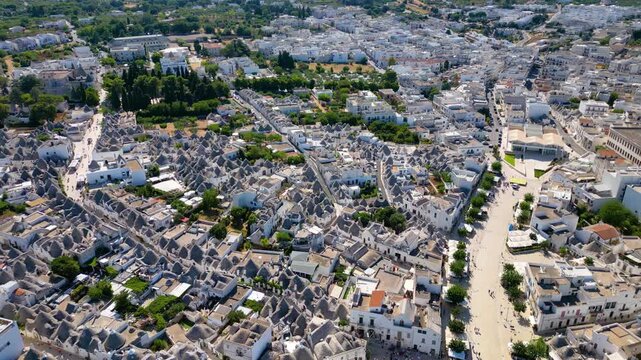 A breathtaking high aerial view of Alberobello in Puglia, Italy, revealing thousands of iconic white trulli huts with conical stone roofs. The historic UNESCO town stretches across the landscape