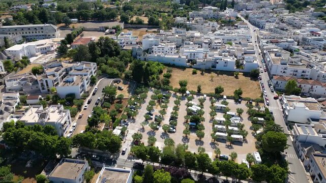 An aerial drone view shows a dedicated camperstop and RV parking area surrounded by olive trees in Alberobello, Italy. The facility sits conveniently right next to the historic UNESCO town filled with