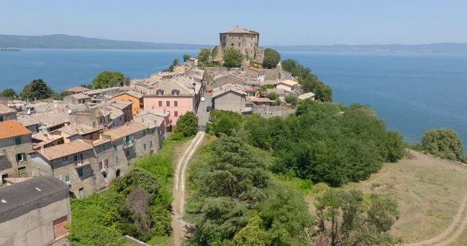 High angle view of the rooftops of Capodimonte with a dirt path through the trees leading to the Rocca Farnese, with the marina and Lake Bolsena behind, in the province of Viterbo, in Lazio, Italy