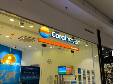 Bright Coral Travel agency storefront with illuminated colorful logo sign, glass entrance and warm interior lighting inside a modern shopping mall corridor