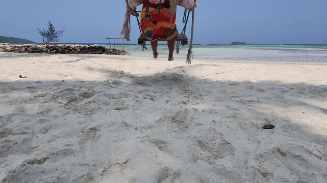 Woman swinging on beach swing at tropical seaside in slow motion, relaxing travel vibes, sunny coastline paradise, vacation getaway, ocean views, leisure lifestyle, holiday movement, peaceful scenery