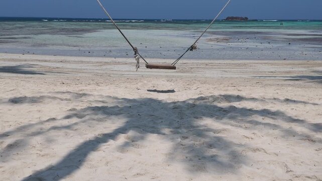 Wooden swing hanging over white sand beach with palm tree shadows in Karimunjawa, peaceful tropical travel destination, relaxing coastal getaway, summer vacation vibes, holiday relaxation scenery