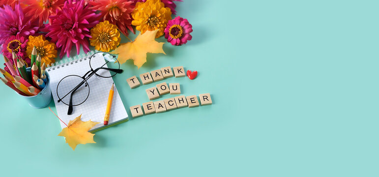 Teacher's day holiday, education concept. Text "Thank you teacher" made of wooden letters, empty notebook, pencils, eyeglass, flowers and autumn maple leaves on table. top view. banner. copy space