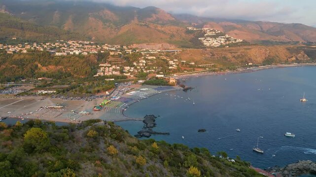 A breathtaking sunset aerial view captures Isola del Dino and the bay at Praia a Mare in Calabria, Italy. Boats navigate the deep blue waters along a sprawling beach, framed by dramatic coastal