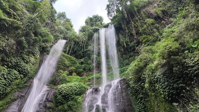 Sekumpul waterfall in Bali featuring cascading water against lush tropical jungle greenery, tranquil nature scenery, pristine forest environment, exotic travel destination. Slow motion