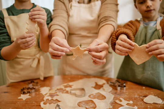 Senior Caucasian woman and children showing raw cookie dough shapes during baking at home, midsection. Concept of intergenerational bonding for holiday cooking advertising