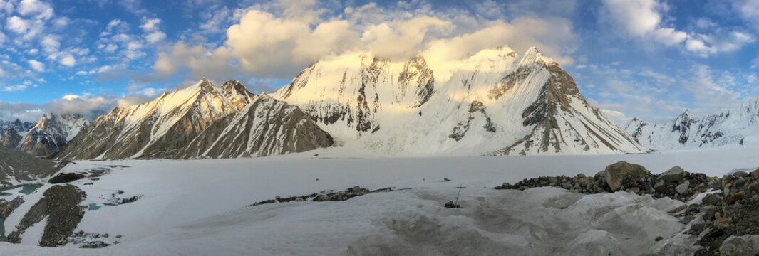 View of Ali Camp K2 with snow-covered peaks of the Karakoram range, glacier ice, and rocky terrain under a blue sky in Skardu, Gilgit, Pakistan.