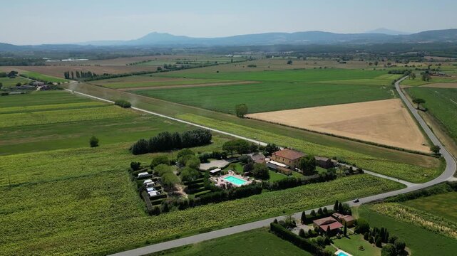 An aerial drone view reveals a charming Tuscan agriturismo nestled among vibrant sunflower fields and vast farmland. The property features a swimming pool and an organized camperstop for motorhomes in