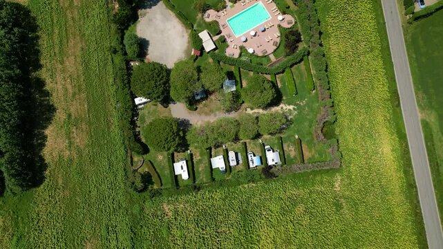 An aerial drone view reveals a charming Tuscan agriturismo nestled among vibrant sunflower fields and vast farmland. The property features a swimming pool and an organized camperstop for motorhomes in