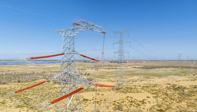 Close-Up Aerial View of High-Voltage Transmission Towers with Orange Insulator Strings on Arid Sandy Land